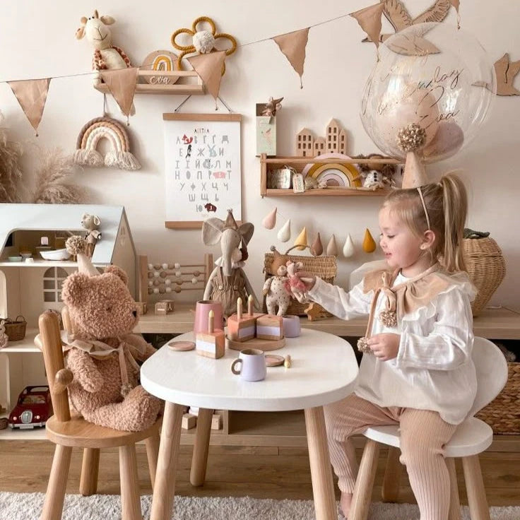 Girl playing with teddy bears and toys at a table in a warm, cozy nursery with Scandinavian decor.