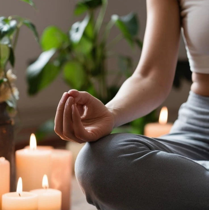 Person meditating with candles and plants, promoting relaxation and health, seated in a yoga pose in a peaceful setting.